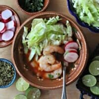 Shrimp Pozole in a clay bowl surrounded by the toppings for the stew.