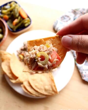A hand holding a chip with Atun a la Veracruzana on it.