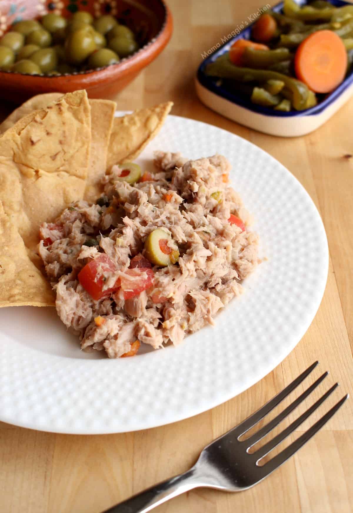Atun a la Veracruzana served on a white plate with chips and pickled jalapenos.