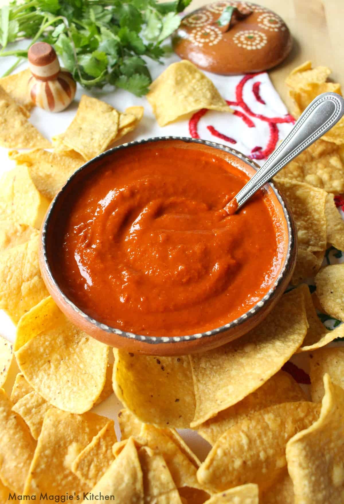 Cascabel Chile Salsa in a bowl with a spoon and surrounded by tortilla chips.