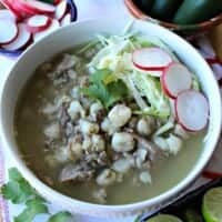 Instant Pot Pork Pozole Verde in a white bowl topped with cilantro, radishes, and cabbage.