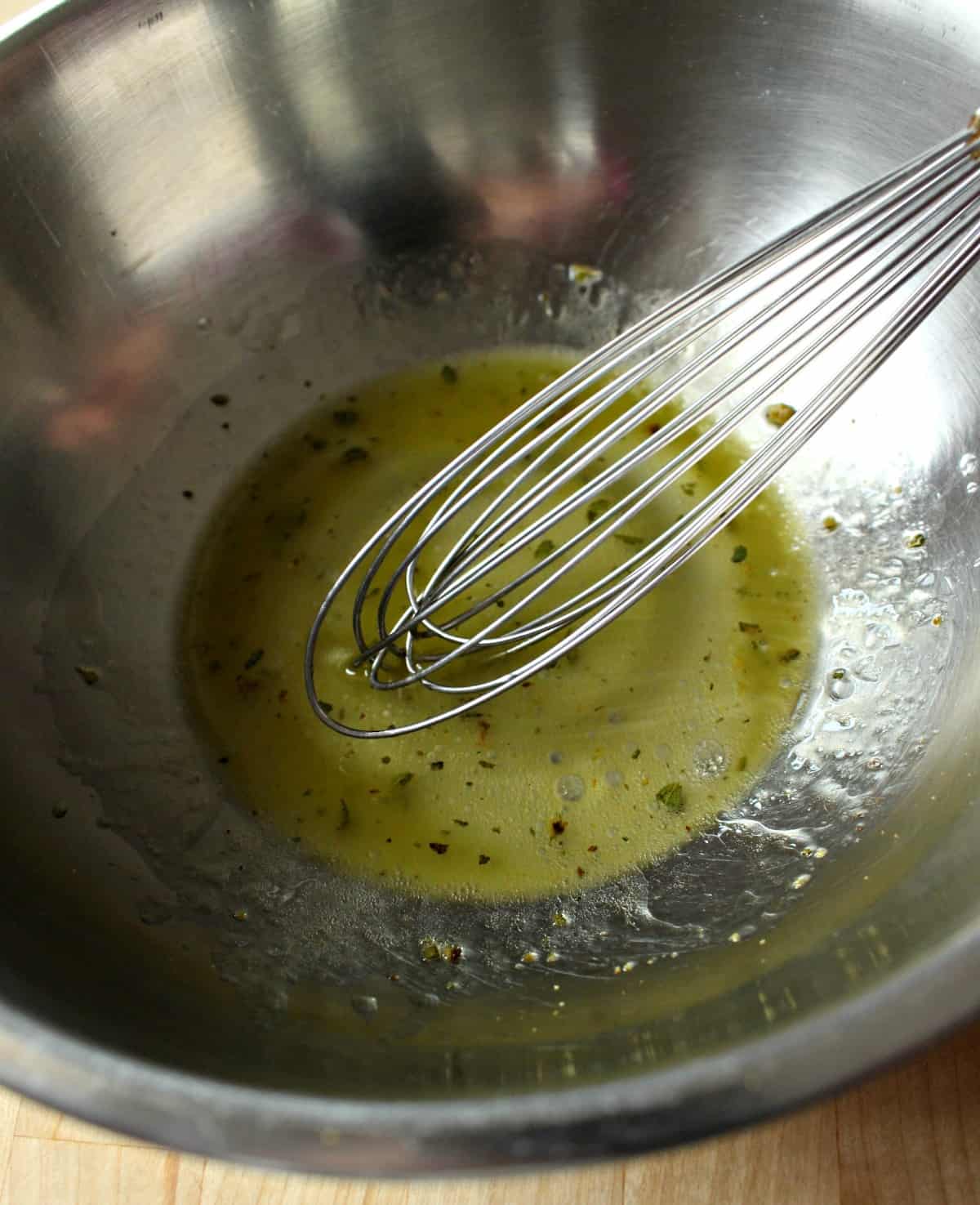 A whisk in a metal bowl making a vinaigrette.