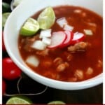 Pozole Rojo in a white bowl topped with radishes and lime wedges.