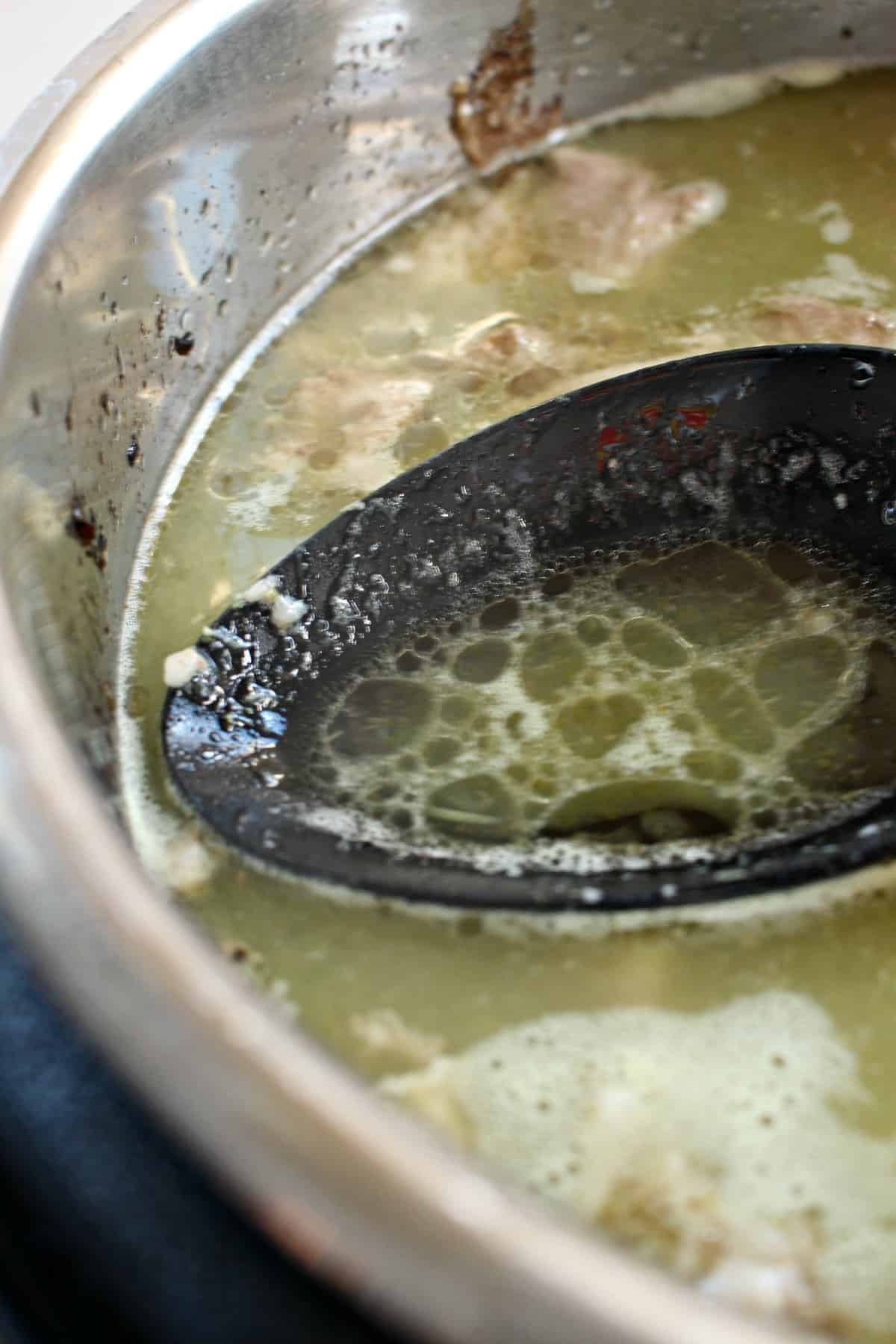 A cooking spoon removing the excess fat from the top of the instant pot.