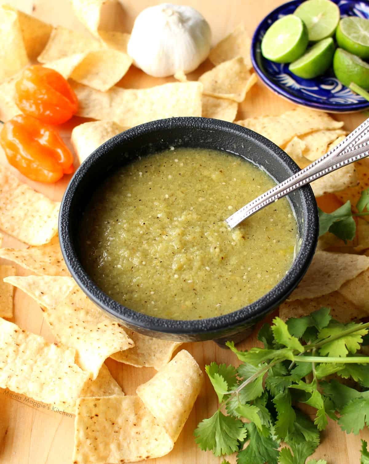 Tomatillo Habanero Salsa in a black bowl surrounded by habaneros and chips.