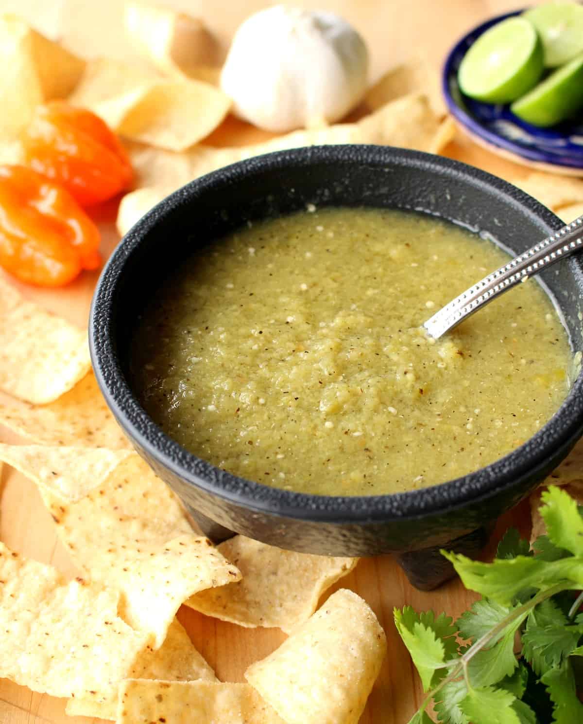 Tomatillo Habanero Salsa in a black bowl surrounded by chips.