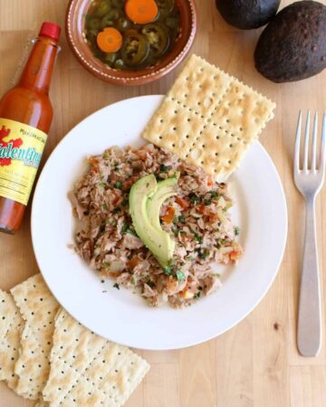 Atun a la Mexicana served with saltine crackers on a white plate and topped with sliced avocado.