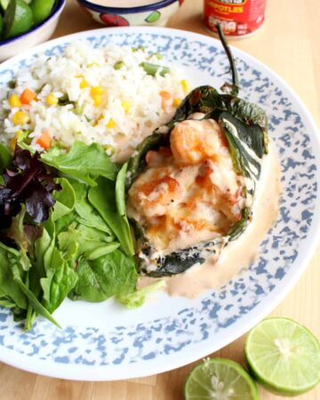 A shrimp chile relleno served on a plate next to a salad and rice.