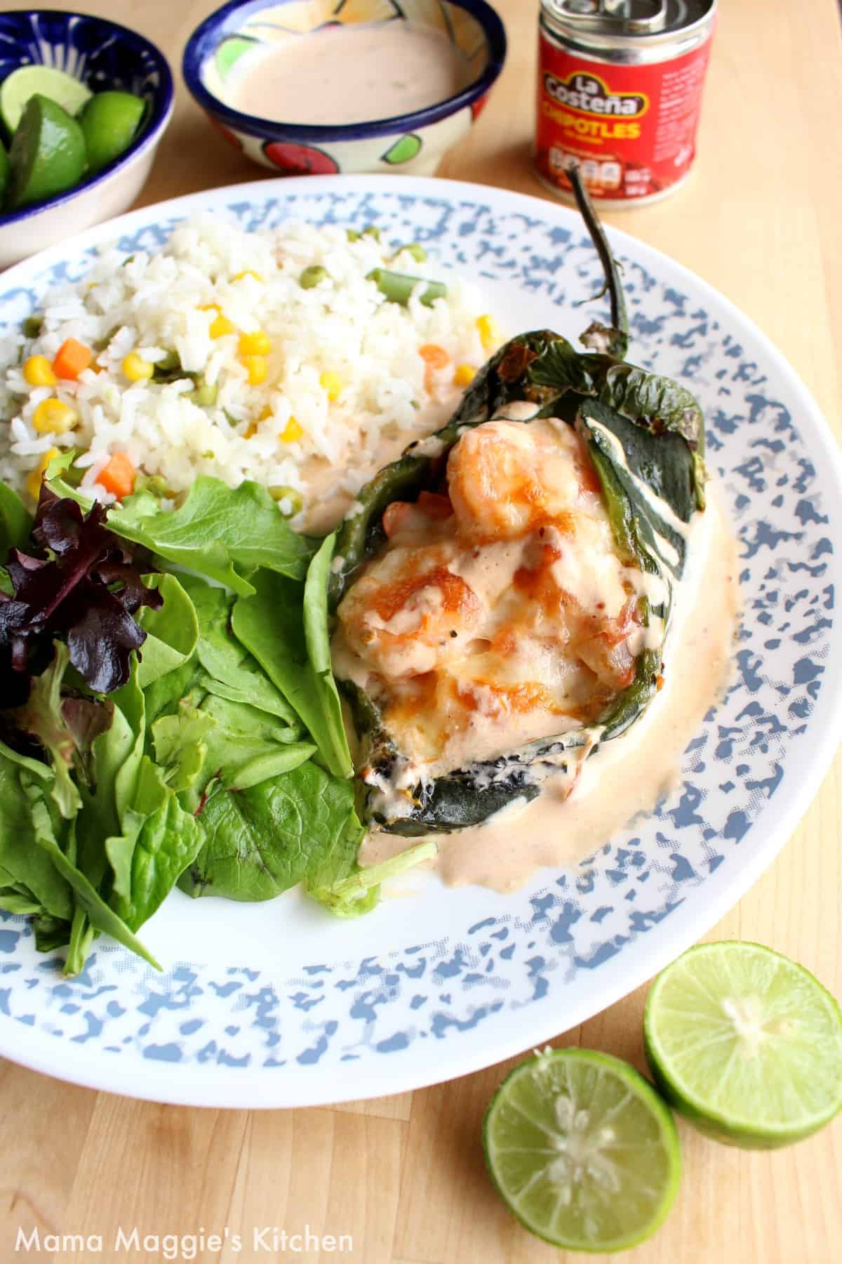 A shrimp chile relleno served on a plate next to a salad and rice.