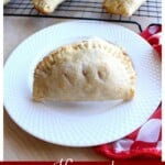 An apple empanada on a white plate next to a red checkered napkin and more empanadas cooling.