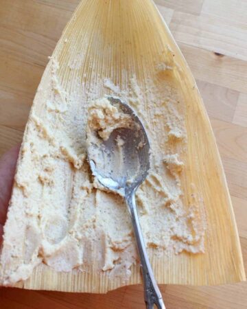 A spoon spreading masa on a corn husk.