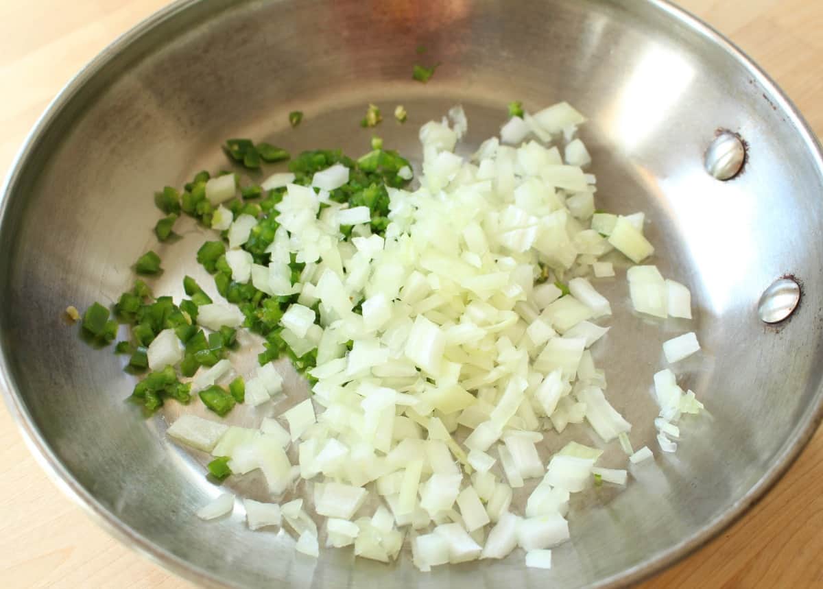 Diced jalapeno and onion cooking in a metal skillet.
