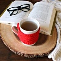 A cup of oregano tea on a wooden surface next to a book and glasses.