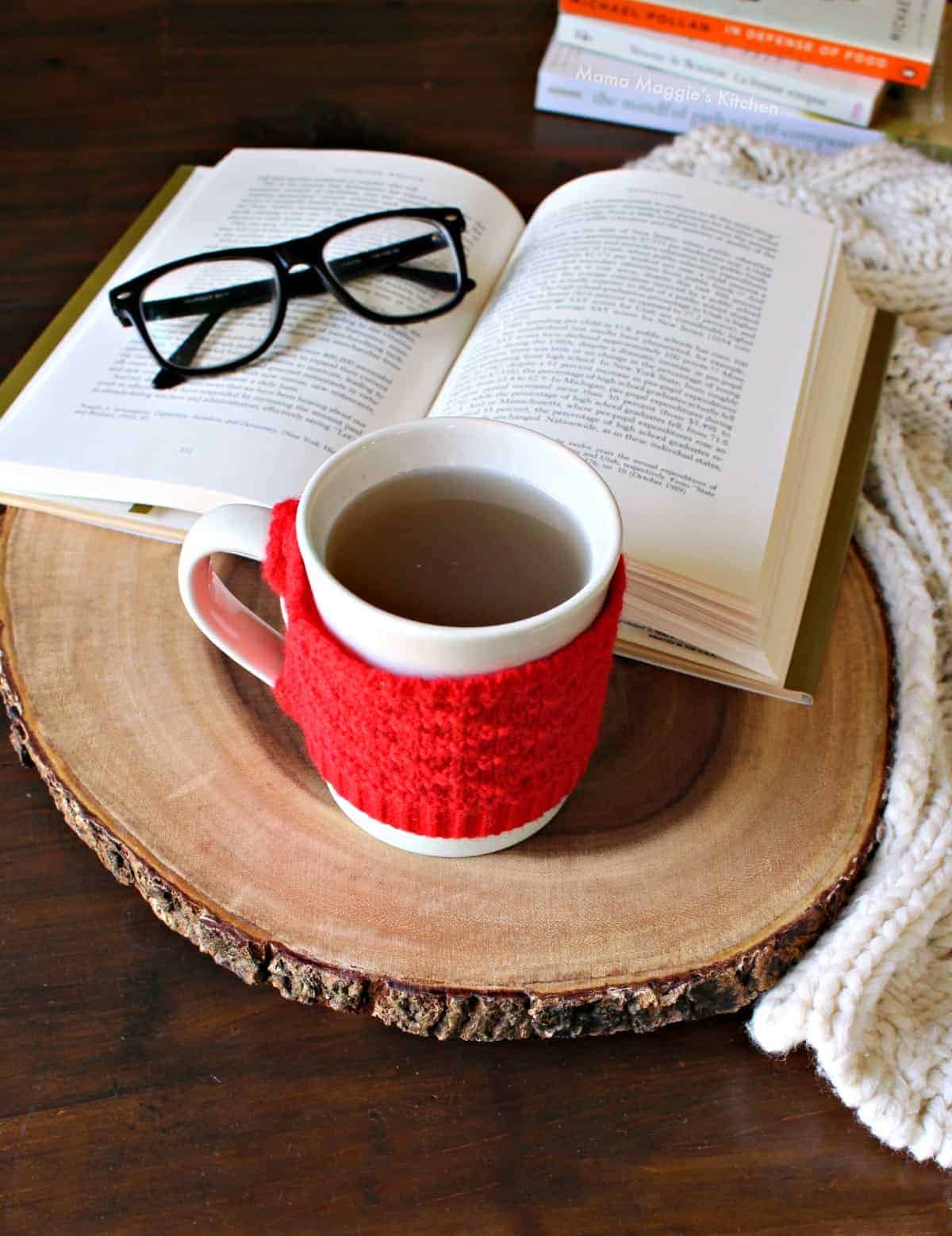 A cup of oregano tea on a wooden surface next to a book and glasses.