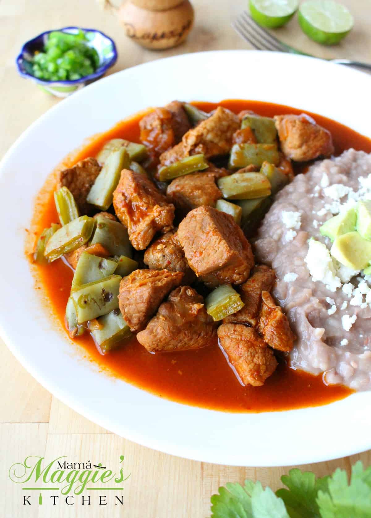 Pork chile colorado with nopales served next to refried beans on a white plate.