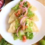Potato Tacos Dorados on a white plate topped with lettuce, tomatoes, and pickled red onions.