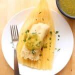A vegetable tamal on top of a corn husk drizzled with green salsa verde and chopped cilantro.