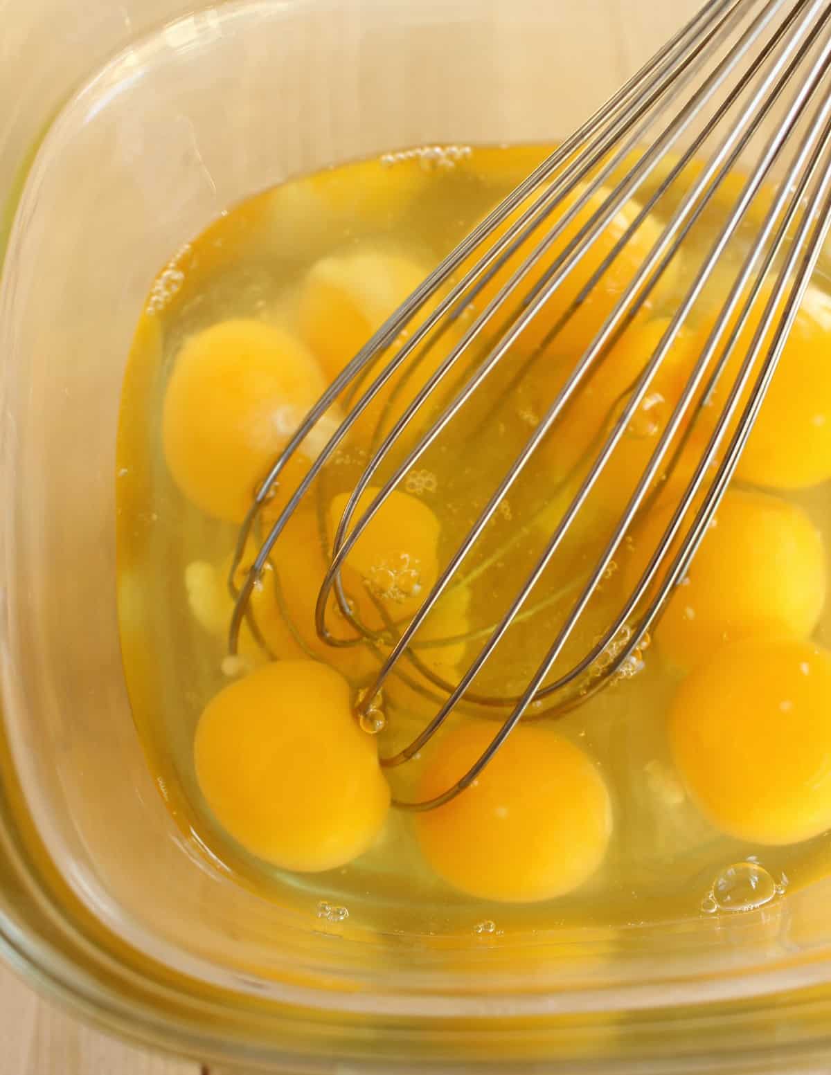 Eggs being whisked in a glass bowl.