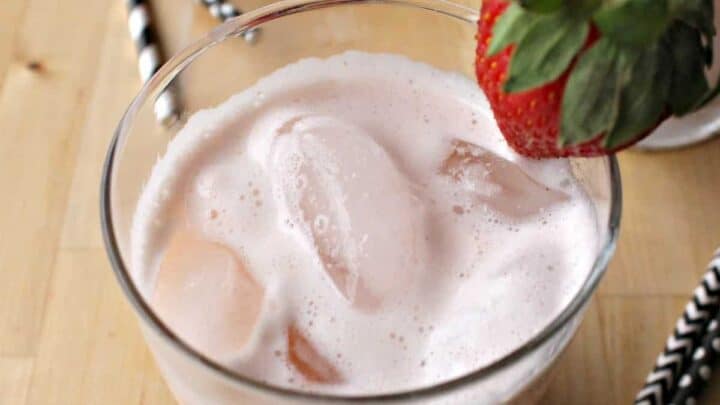 A glass of Agua de Fresa topped with a whole strawberry next to straws.