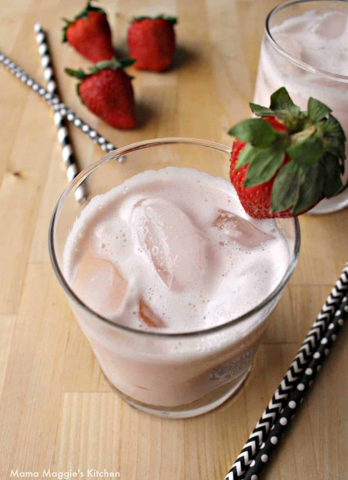 A glass of Agua de Fresa topped with a whole strawberry next to straws.