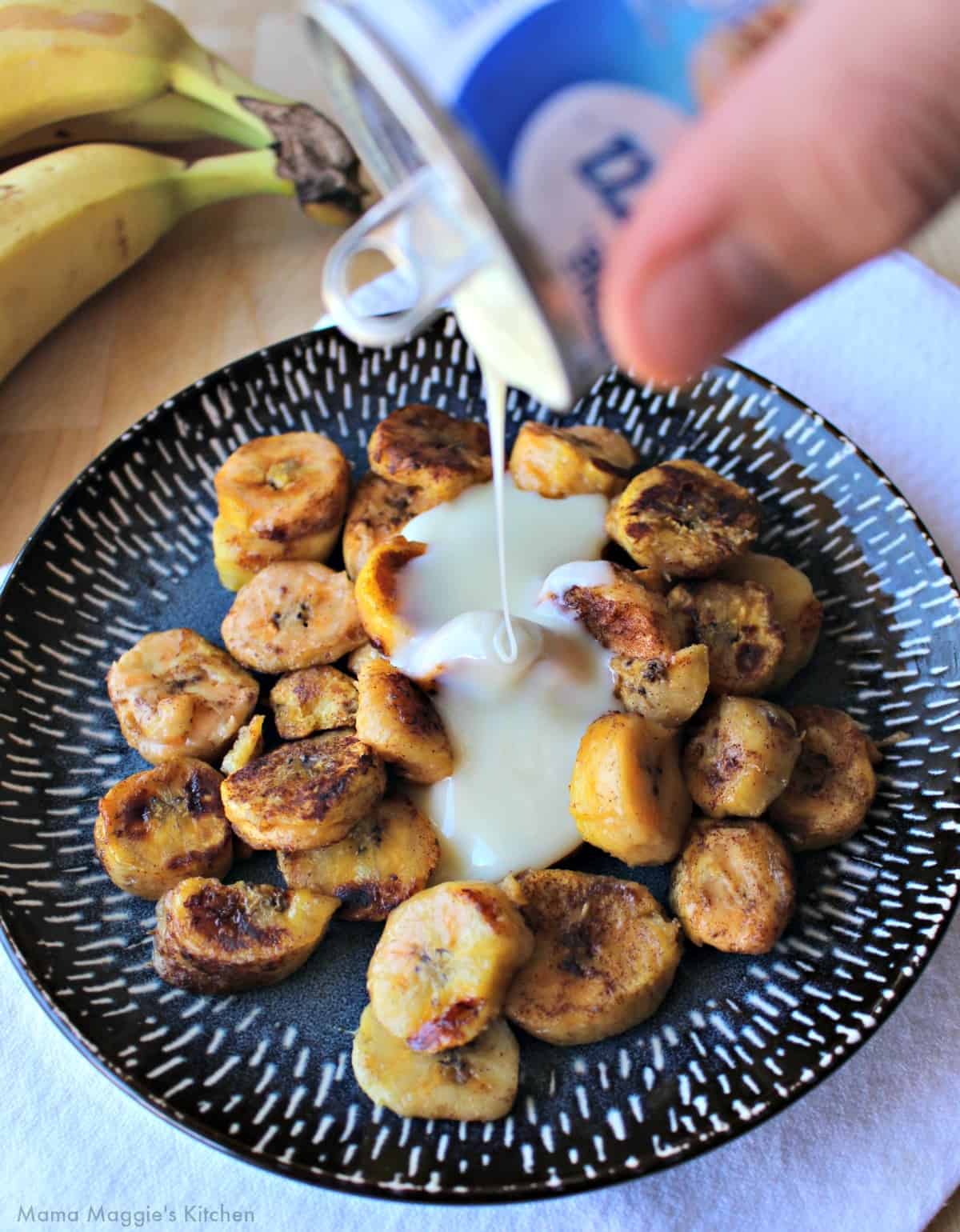 A hand holding a container of sweetened and drizzling it over the fried bananas.