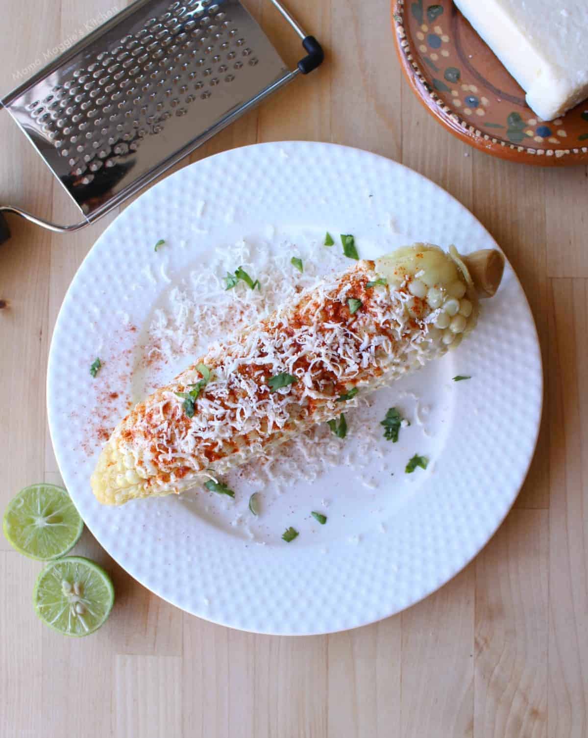 Elote Mexicano (or Mexican Street Corn) on a white plate topped with chile powder, cheese, and cilantro.