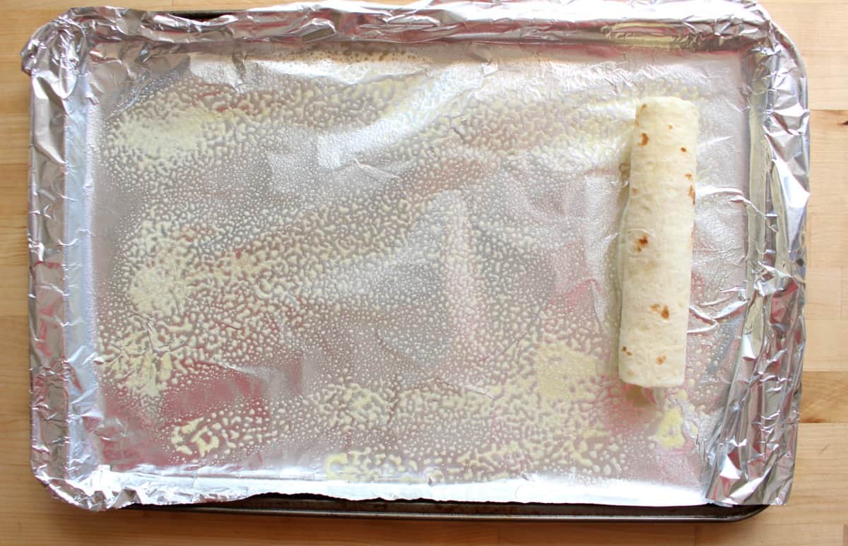 An unbaked flauta on a cookie sheet.