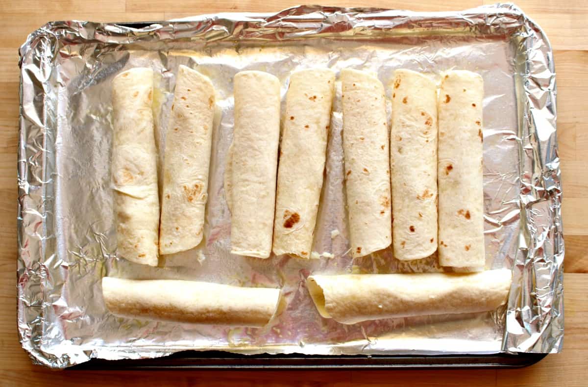 Unbaked flautas lined up on a cookie sheet.
