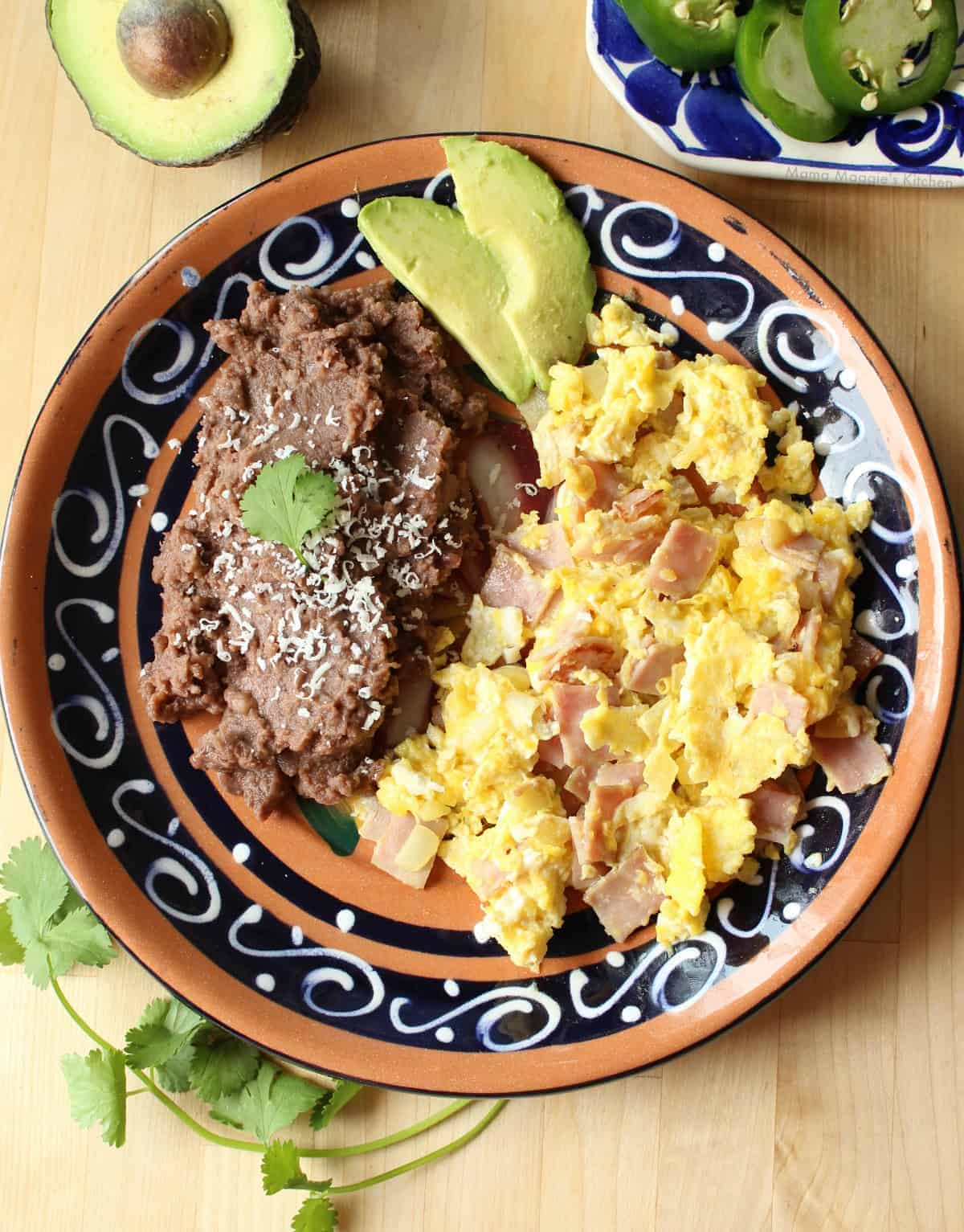 Huevos con Jamon served on a plate with a side of beans and slices of avocado.