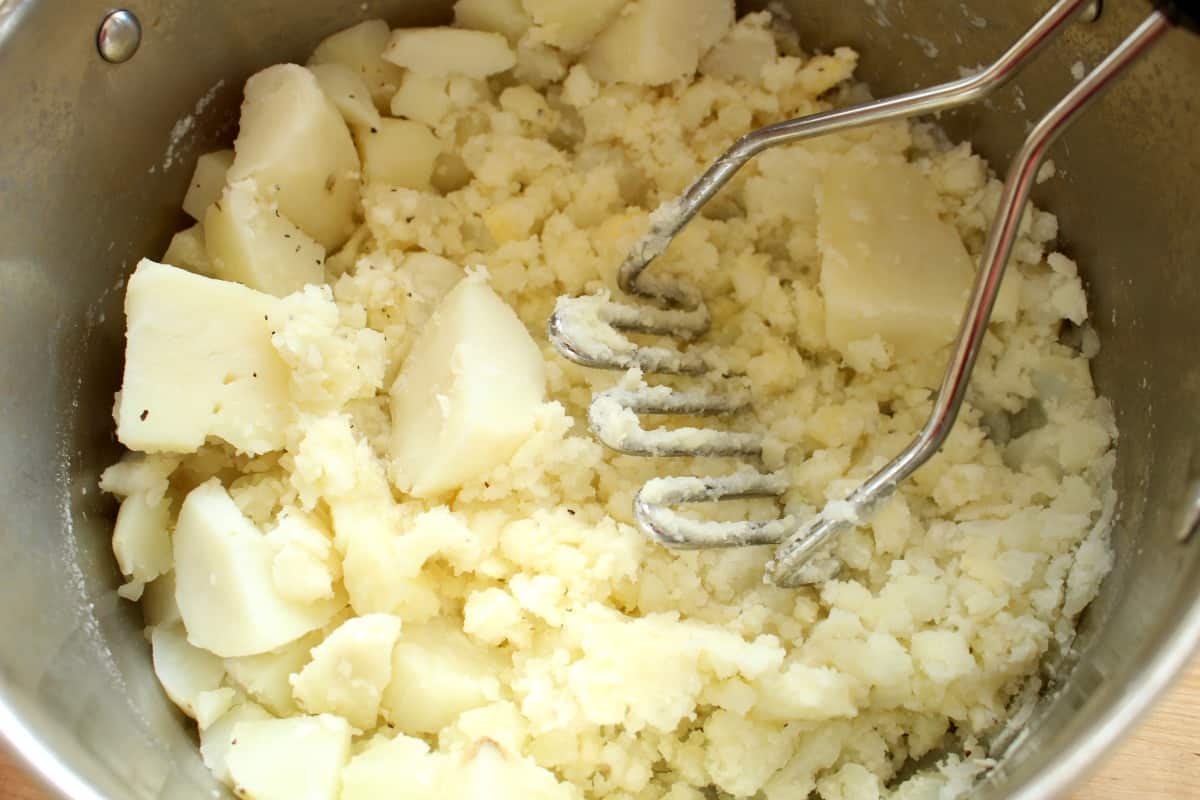 A potato masher in a pot mashing cooked potatoes.
