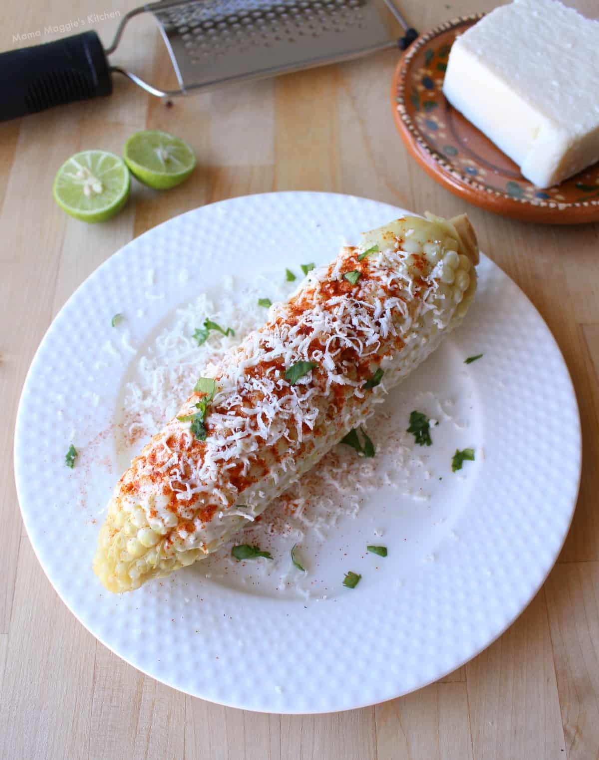 Mexican street corn on top of a white plate and topped with chopped cilantro, cheese, and chile powder.