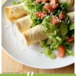 Vegan potato flautas on a white plate topped with lettuce and tomatoes.