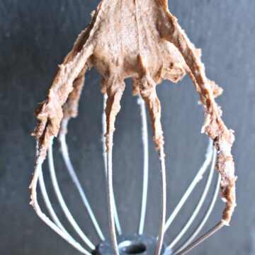 A hand holding a mixer attachment with covered with Abuelita Chocolate Frosting.