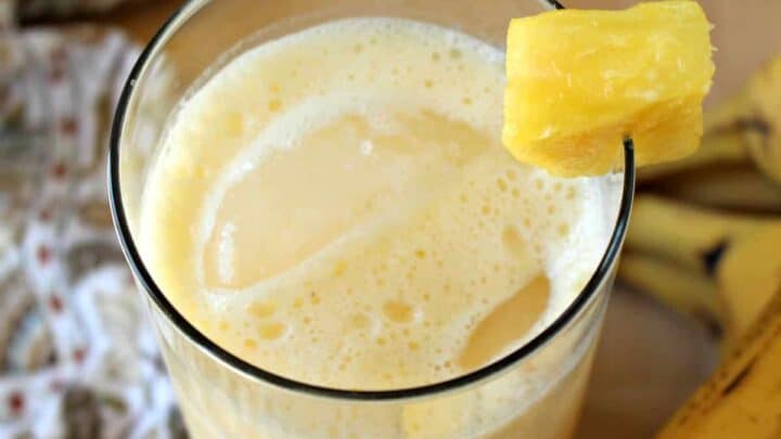A glass of pineapple banana agua fresca decorated with a pineapple wedge and surrounded by bananas.