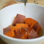 The candied syrup drizzling over the sweet potatoes in a white bowl.