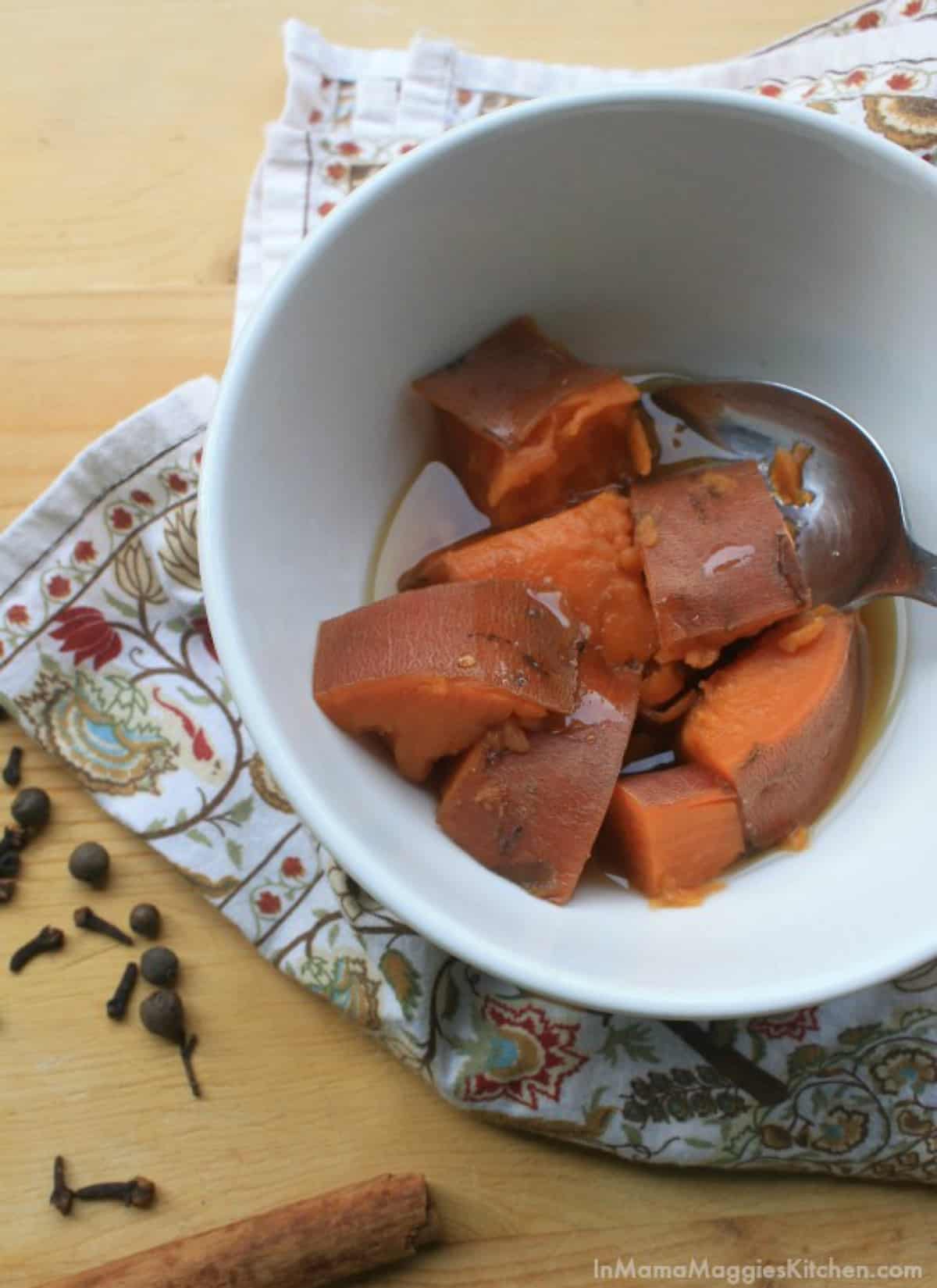 A white bowl with sweet potatoes and a spoon.