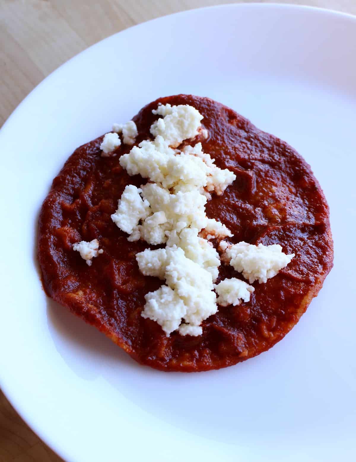 A tortilla that is covered with red sauce and crumbled cheese in the center.