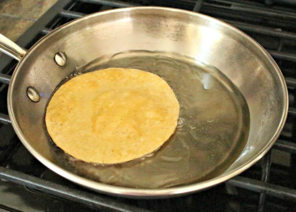 A tortilla frying in a metal skillet.