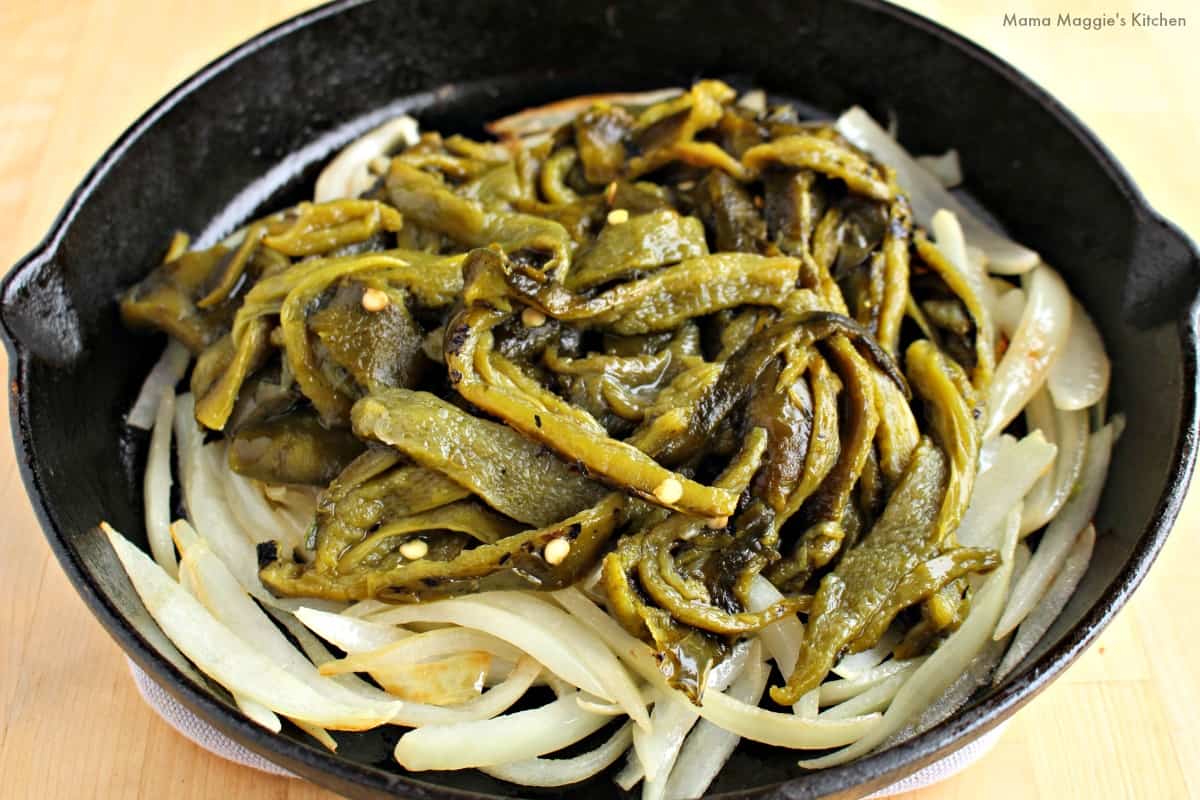 A black iron skillet with onion and slices of roasted poblano pepper.