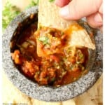 Hand holding a chip with salsa chile piquin over a molcajete.