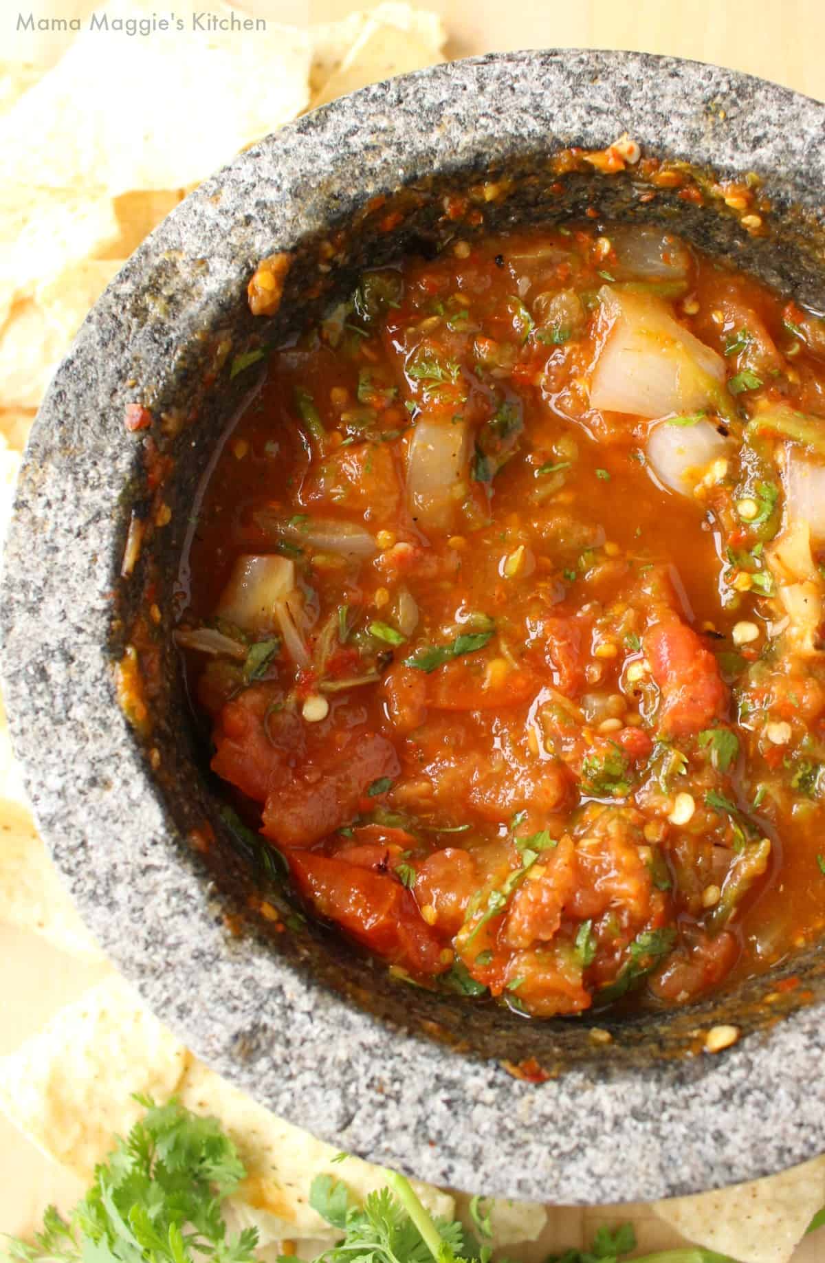 Salsa Chile Piquin in a molcajete surrounded by tortilla chips and green cilantro.