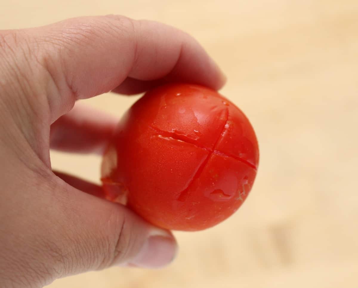 A hand holding a tomato with a criss cut on the bottom.
