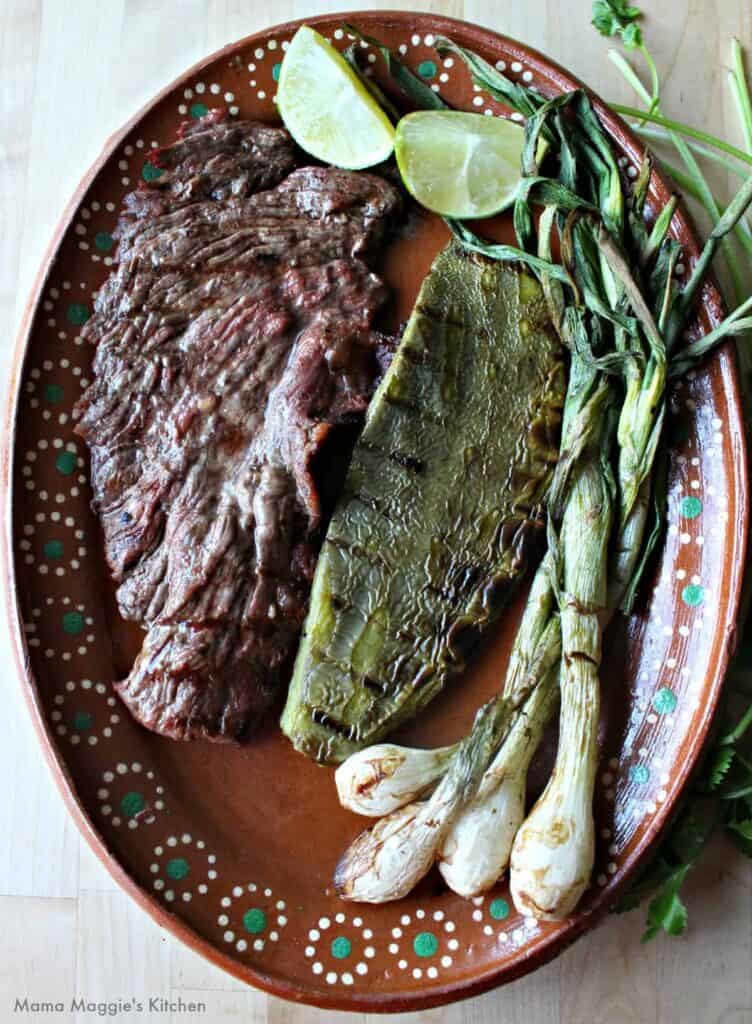 Carne asada, grilled cactus and spring onions on a decorative clay plate.