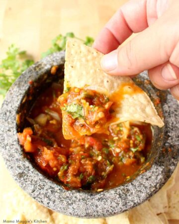Hand holding a chip with salsa chile piquin over a molcajete.