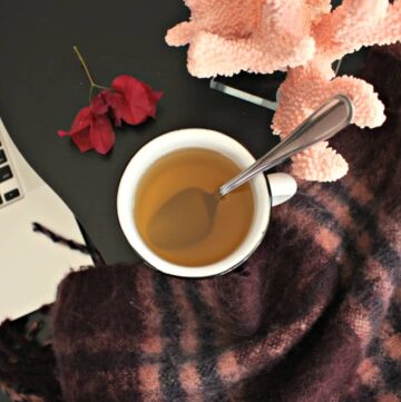 A white cup with Bougainvillea tea next to a wool scarf and a computer.