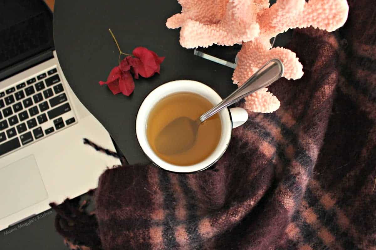 A white cup with Bougainvillea tea next to a wool scarf and a computer.