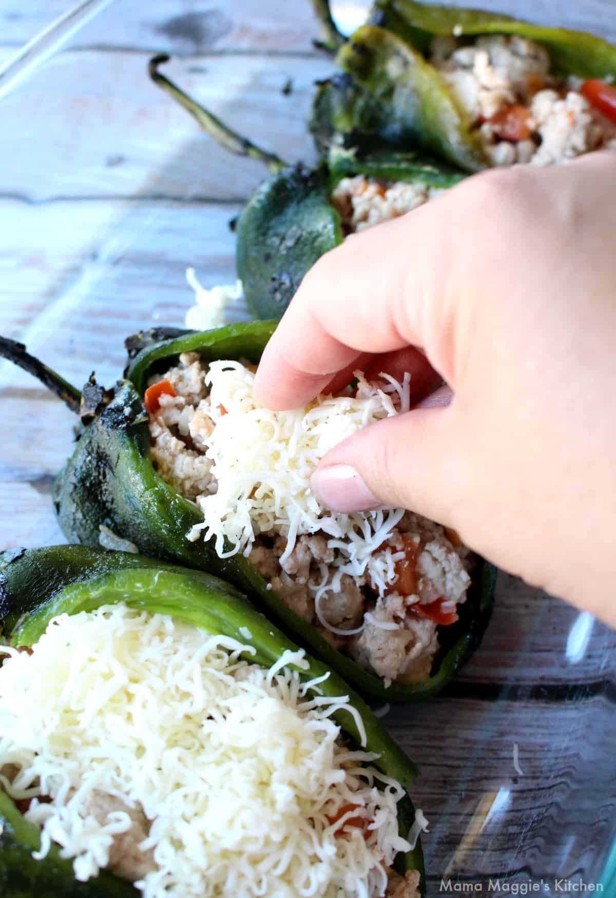 A hand adding grated cheese on top of a stuffed poblano. 