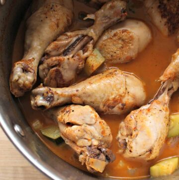 Chicken legs swimming in guajillo sauce in a stock pot.