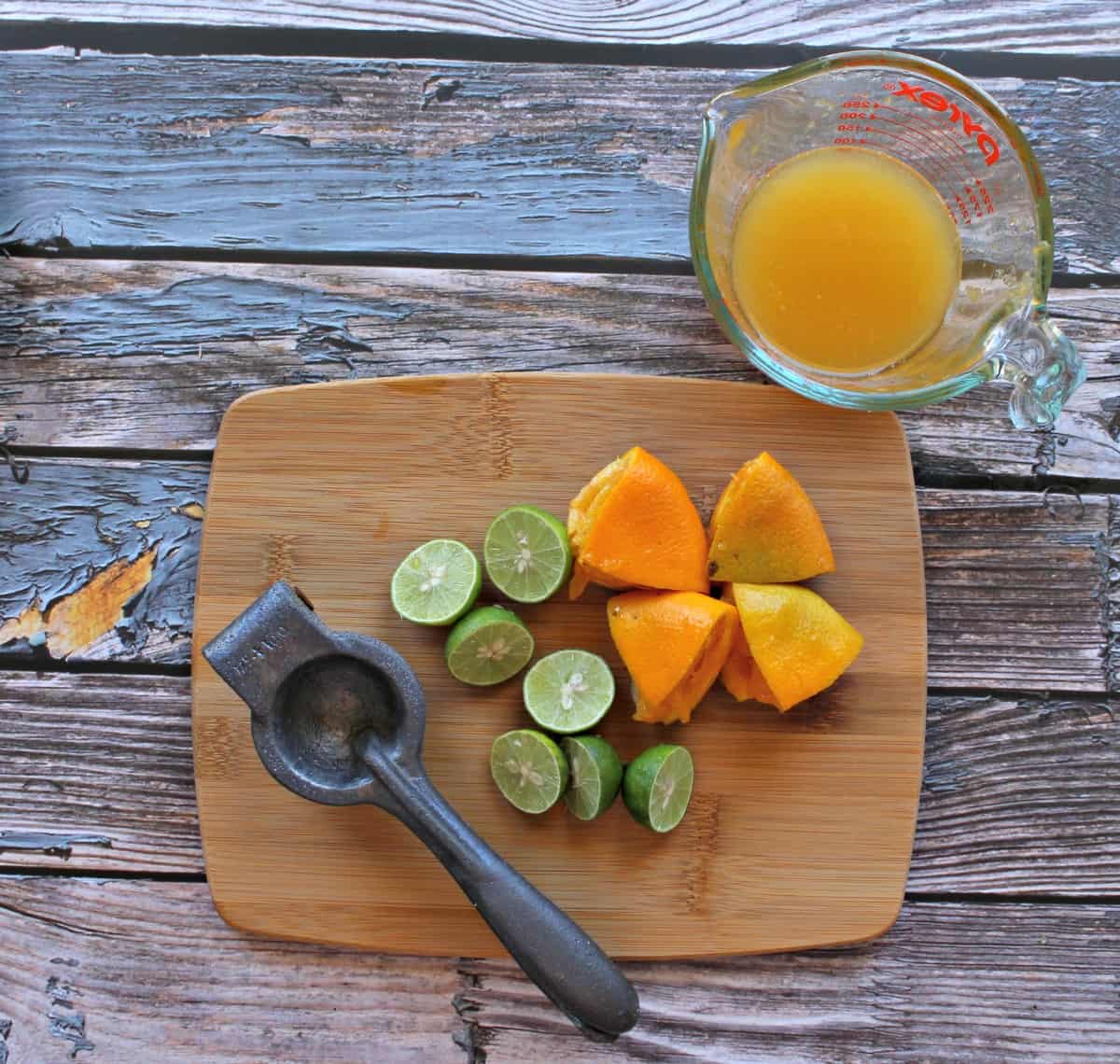 A citrus juicer, lime wedges, and orange wedges on a cutting board next to freshly squeezed orange juice.