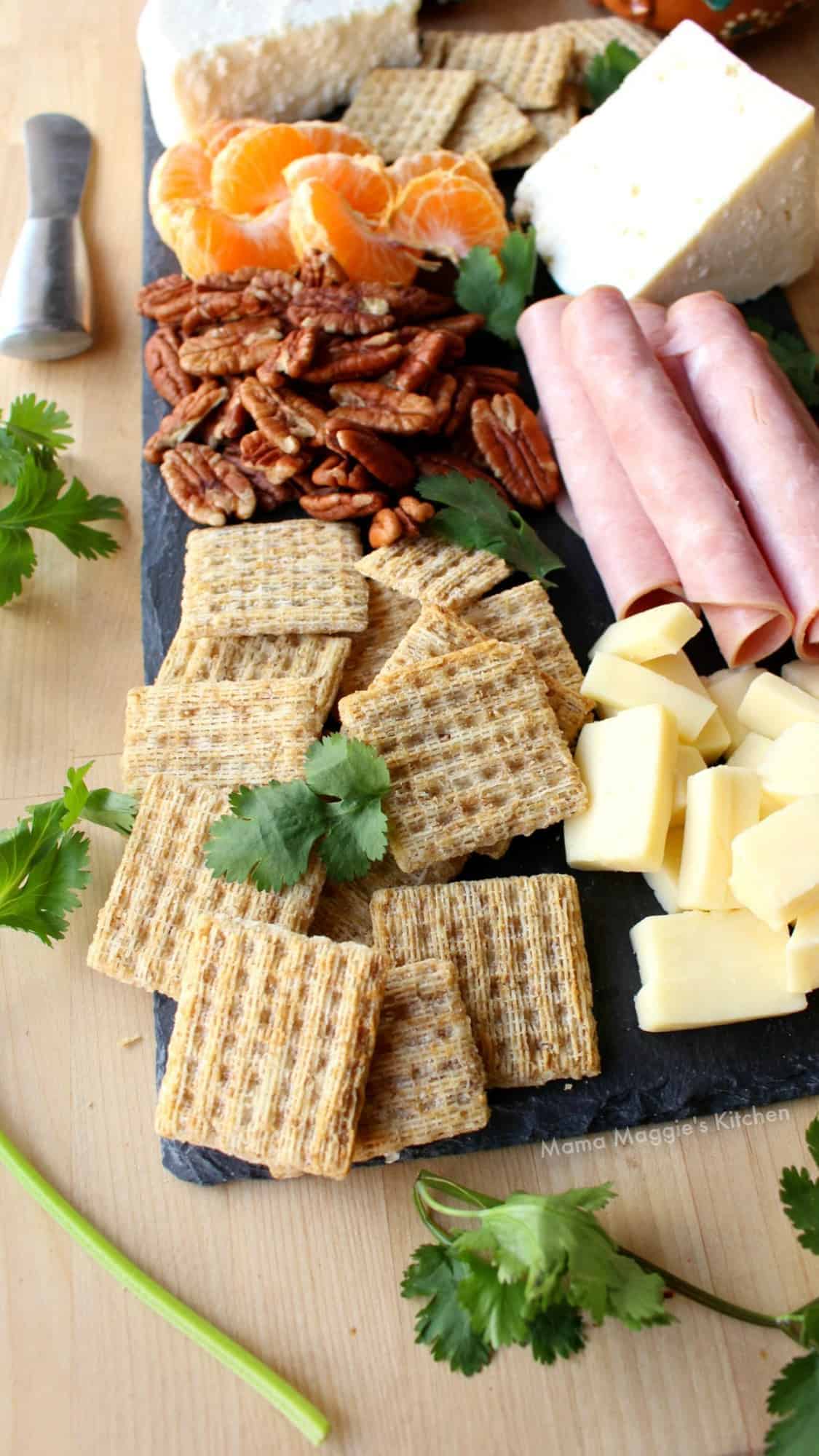 Triscuits on a Mexican Charcuterie board next to guacamole, con salsa, olives, and different kinds of Mexican cheeses.